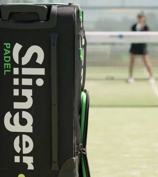 Slinger Bag padel ball launcher in black and green on indoor padel court
