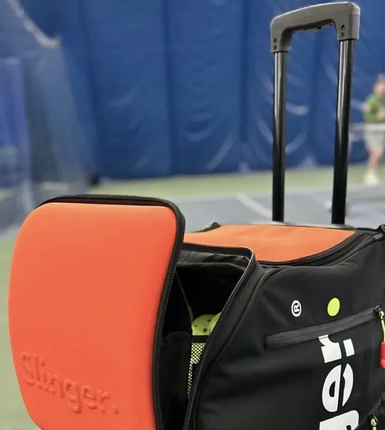 Slinger Bag pickleball launcher with orange ball hopper on outdoor court