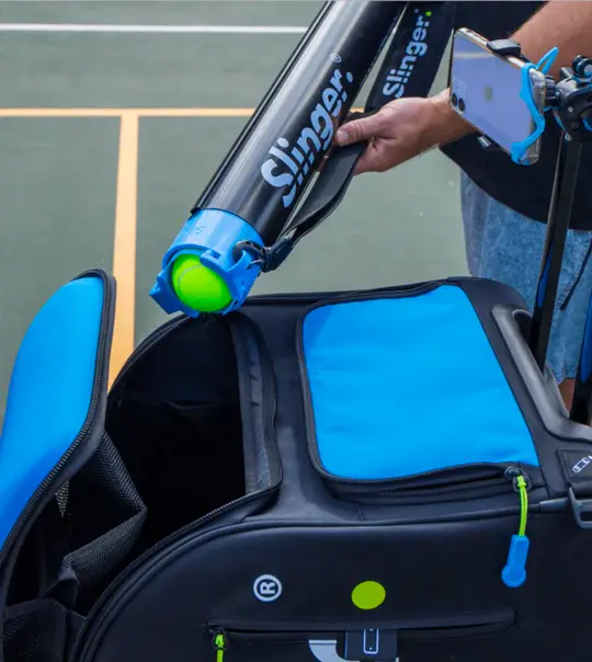 Slinger Bag tennis ball launcher in blue showing feeding mechanism and tennis balls